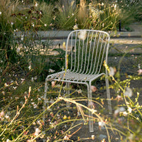 "White metal chair in a garden surrounded by wildflowers, featuring a minimalistic, modern design with vertical lines."