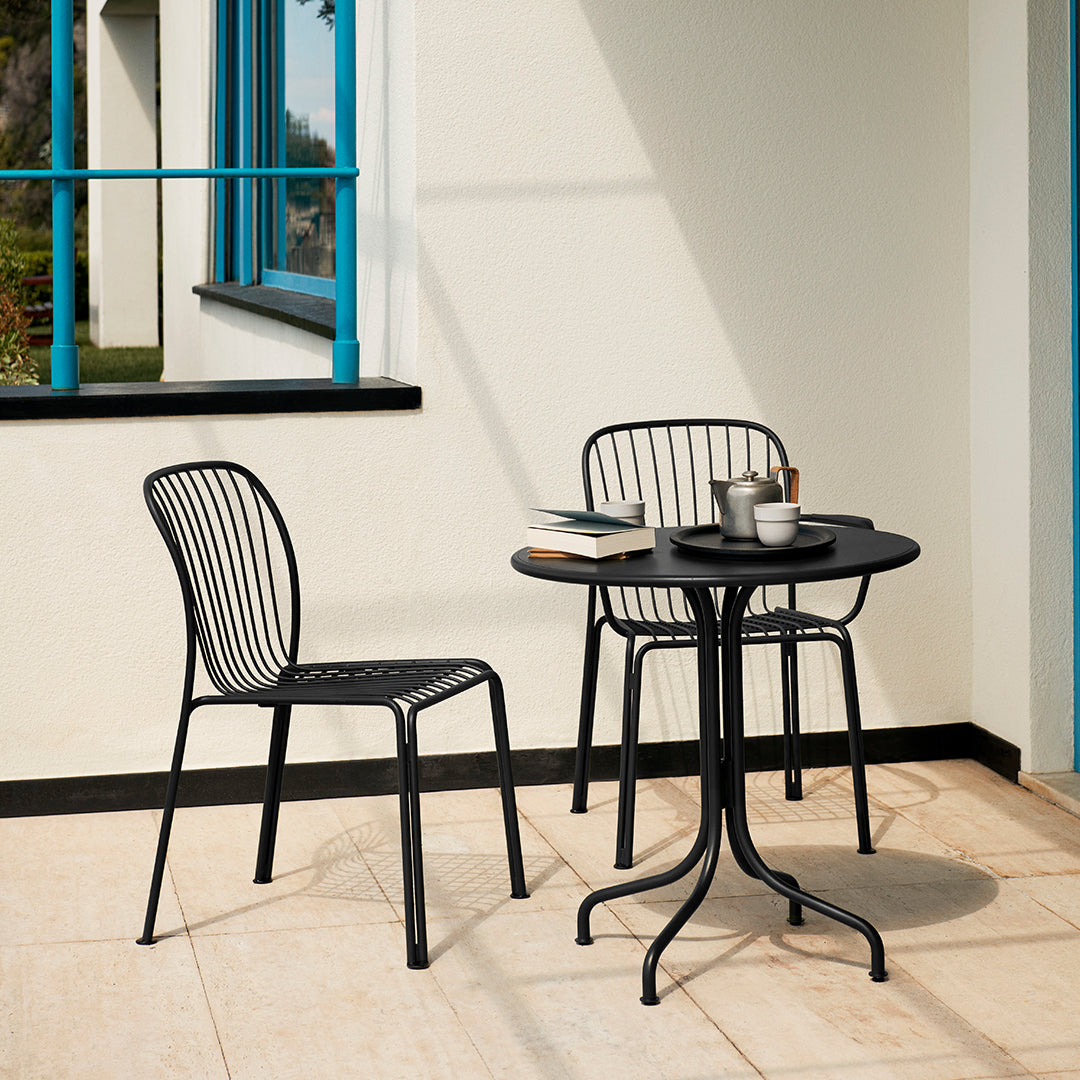 Black metal chairs and table with sleek lines, set against a light-colored patio with blue window accents.