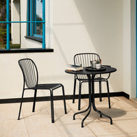 Black metal chairs and table with sleek lines, set against a light-colored patio with blue window accents.