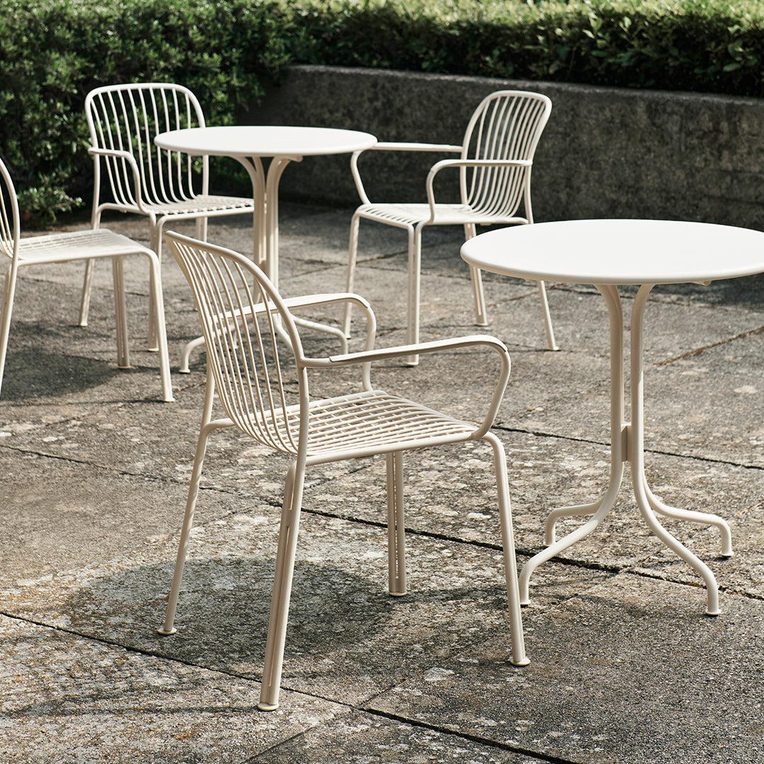 Light beige outdoor chairs and table with a sleek wire design, set against a textured stone surface and greenery.