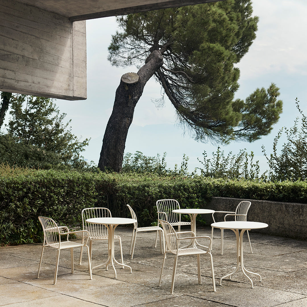 White metal patio furniture with simple lines, set against green foliage and a gray concrete background.