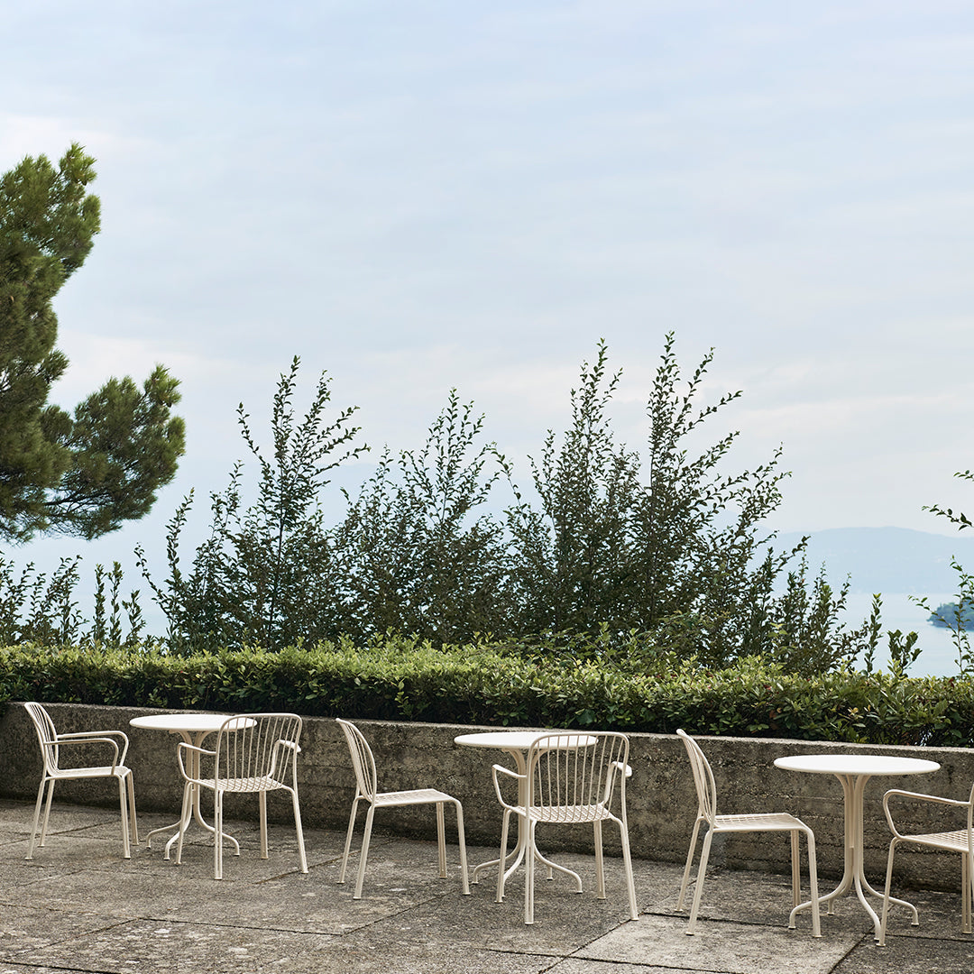 "White outdoor chairs with minimalist design against a backdrop of greenery and soft blue sky."
