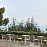 "White outdoor chairs with minimalist design against a backdrop of greenery and soft blue sky."