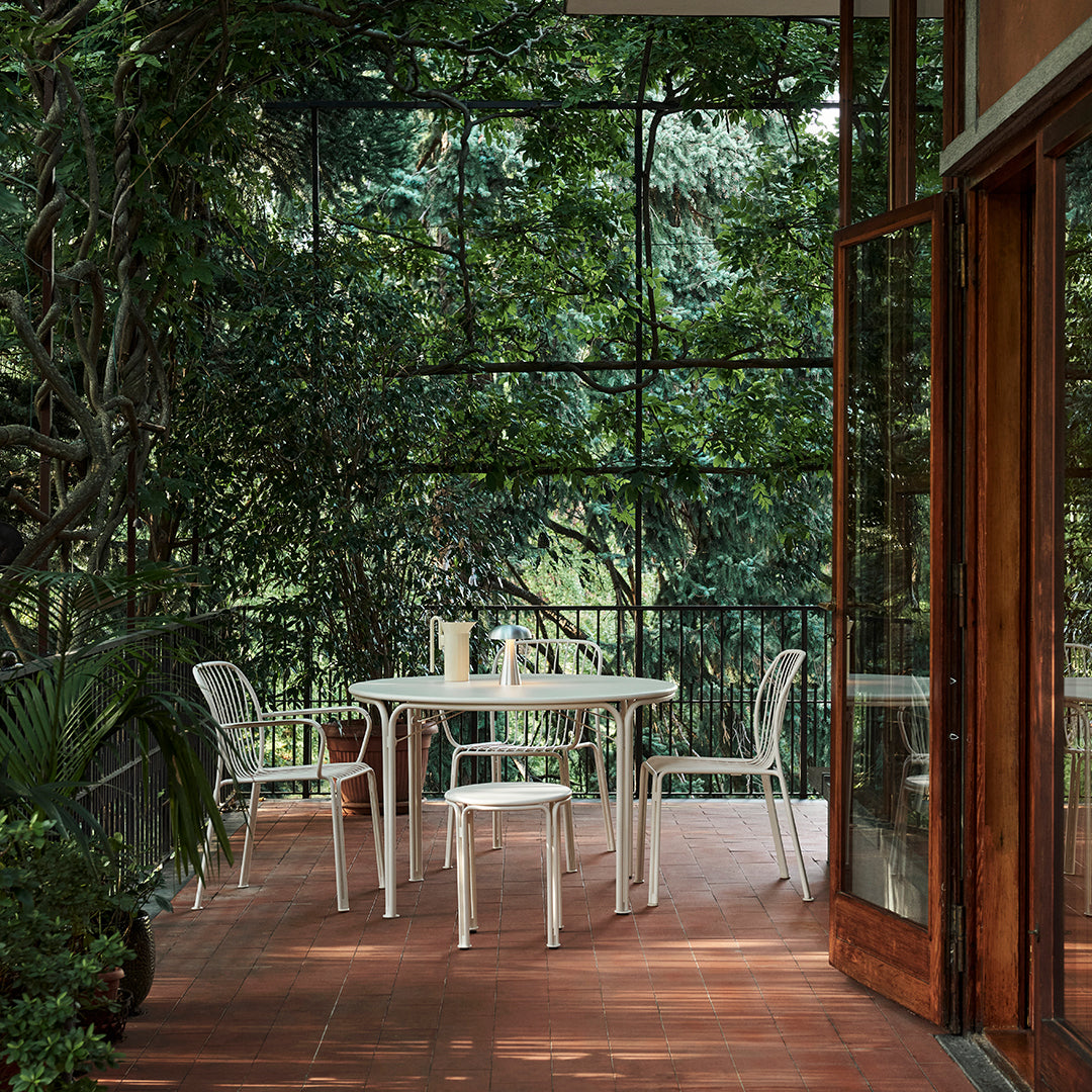 Modern white patio furniture on a terracotta floor, surrounded by lush green foliage and natural light.