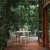 Modern white patio furniture on a terracotta floor, surrounded by lush green foliage and natural light.