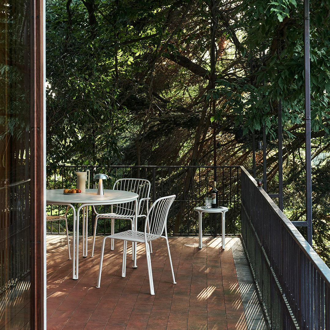 White metal outdoor furniture set against lush greenery, complemented by a warm terracotta floor. Modern design and textures.