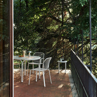 White metal outdoor furniture set against lush greenery, complemented by a warm terracotta floor. Modern design and textures.