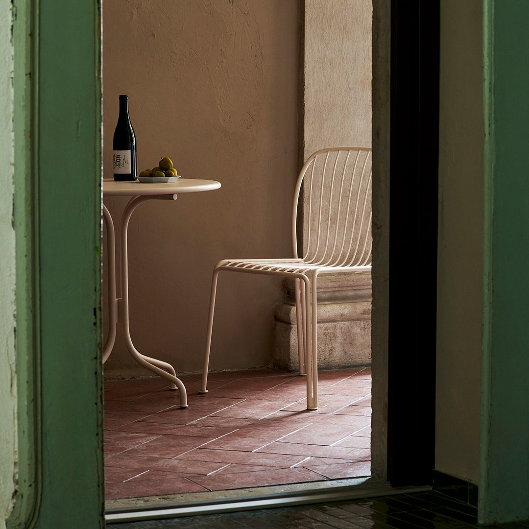 Neutral-toned, woven chair with a round table; soft textures on rustic terracotta flooring and muted walls.
