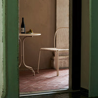 Neutral-toned, woven chair with a round table; soft textures on rustic terracotta flooring and muted walls.