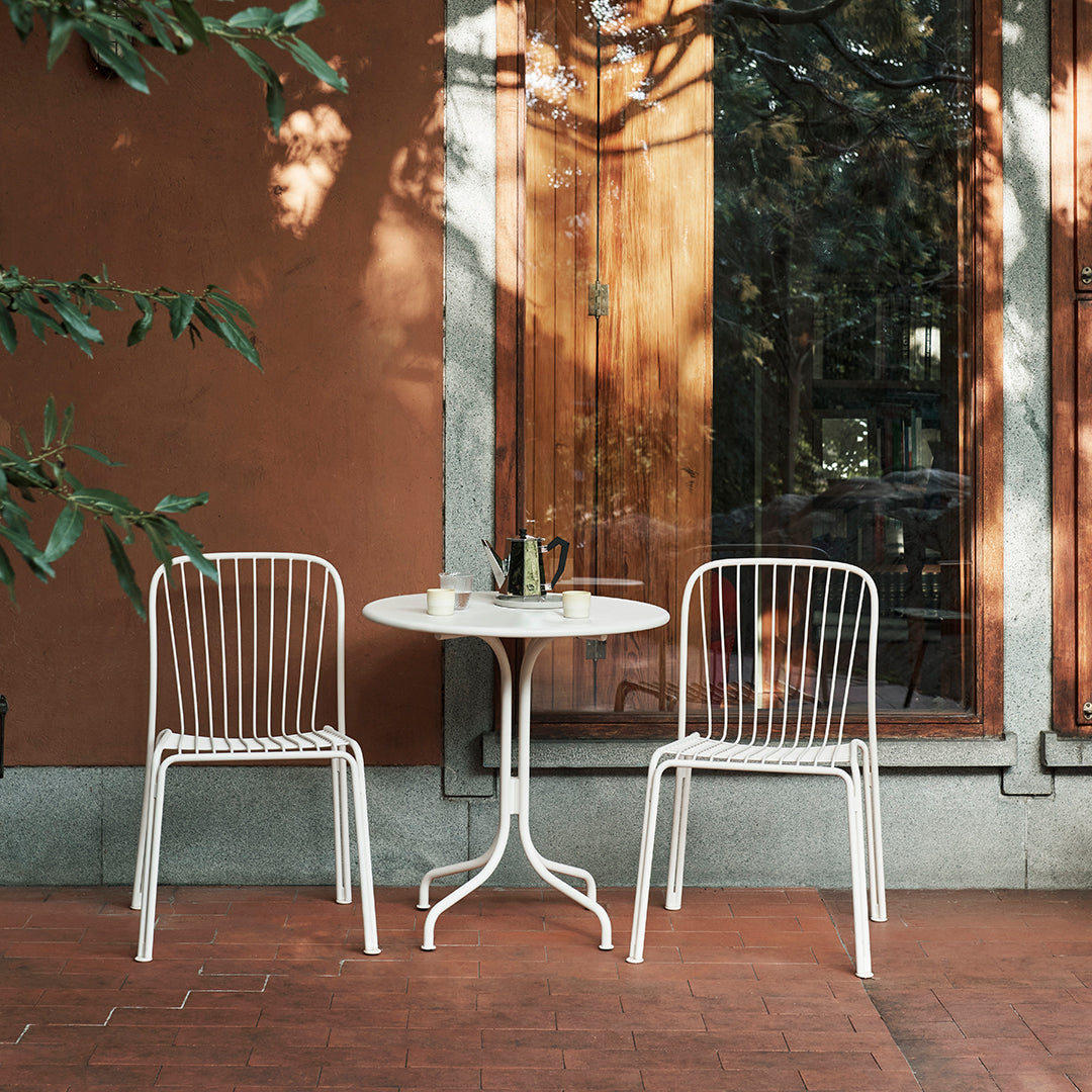White metal chairs and table set against a warm terracotta wall, creating a stylish outdoor dining scene.