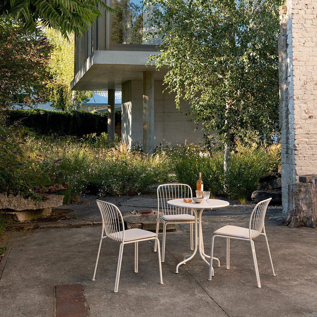 Stylish white patio furniture set featuring a round table and four chairs against a natural green backdrop.