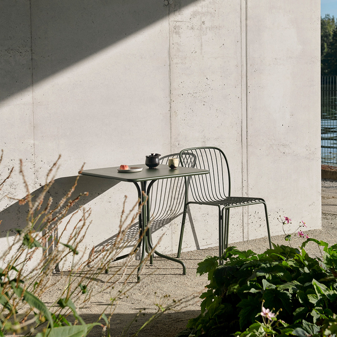 Modern green metal table and chair set with sleek lines, paired against a neutral concrete wall. Perfect outdoor decor!