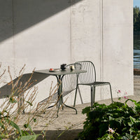 Modern green metal table and chair set with sleek lines, paired against a neutral concrete wall. Perfect outdoor decor!