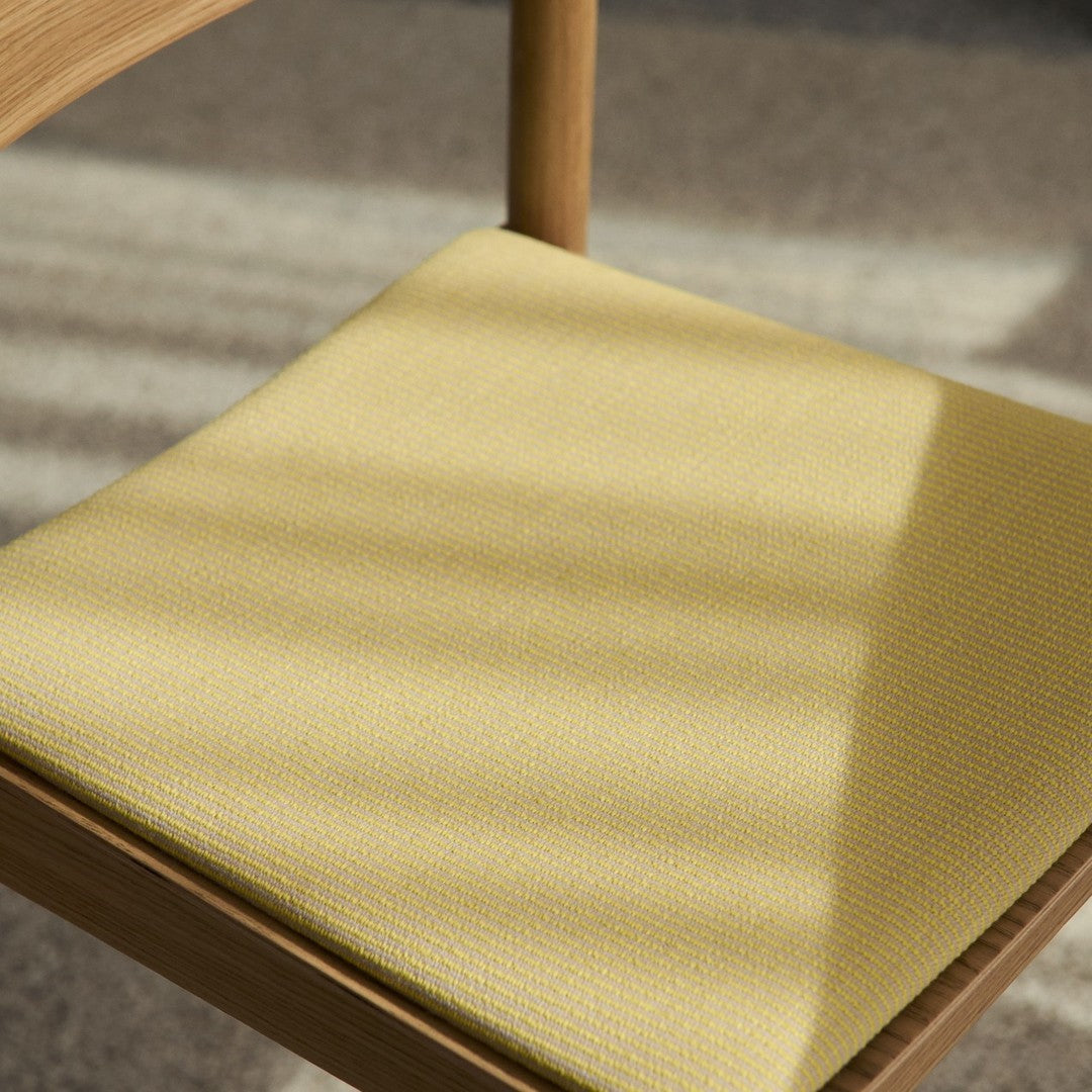 Close-up of a textured yellow chair cushion, featuring subtle patterns and warm wooden accents.
