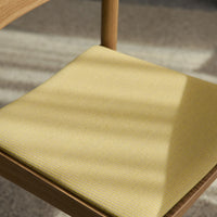 Close-up of a textured yellow chair cushion, featuring subtle patterns and warm wooden accents.