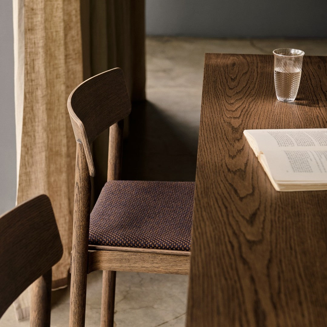 Wooden table with a dark oak finish, complemented by a textured purple and brown patterned chair cushion.
