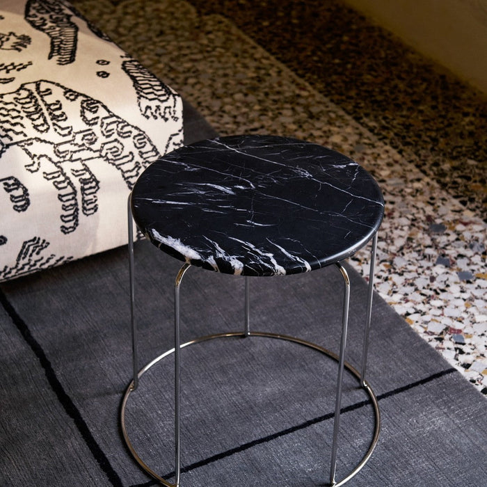 Round black marble side table with white veining, set on a grey patterned rug. Stylish and modern accent piece.