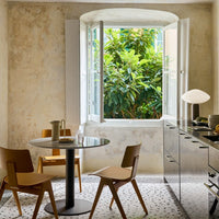 Modern kitchen featuring neutral walls, black table, wooden chairs, and green foliage visible through white windows.