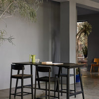 Black wooden bar stools with a sleek, minimalist design against a light gray wall and green accents.