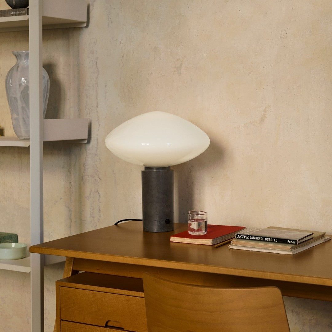 Modern table lamp with a white glass shade, black base, and warm wood tones, set against a textured neutral wall.