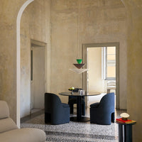 Modern dining area with gray upholstered chairs, a round black table, and a geometric pendant lamp in green and brown tones.