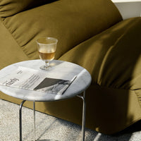 Olive green sofa with textured fabric, white marble table, and a patterned glass filled with amber liquid.