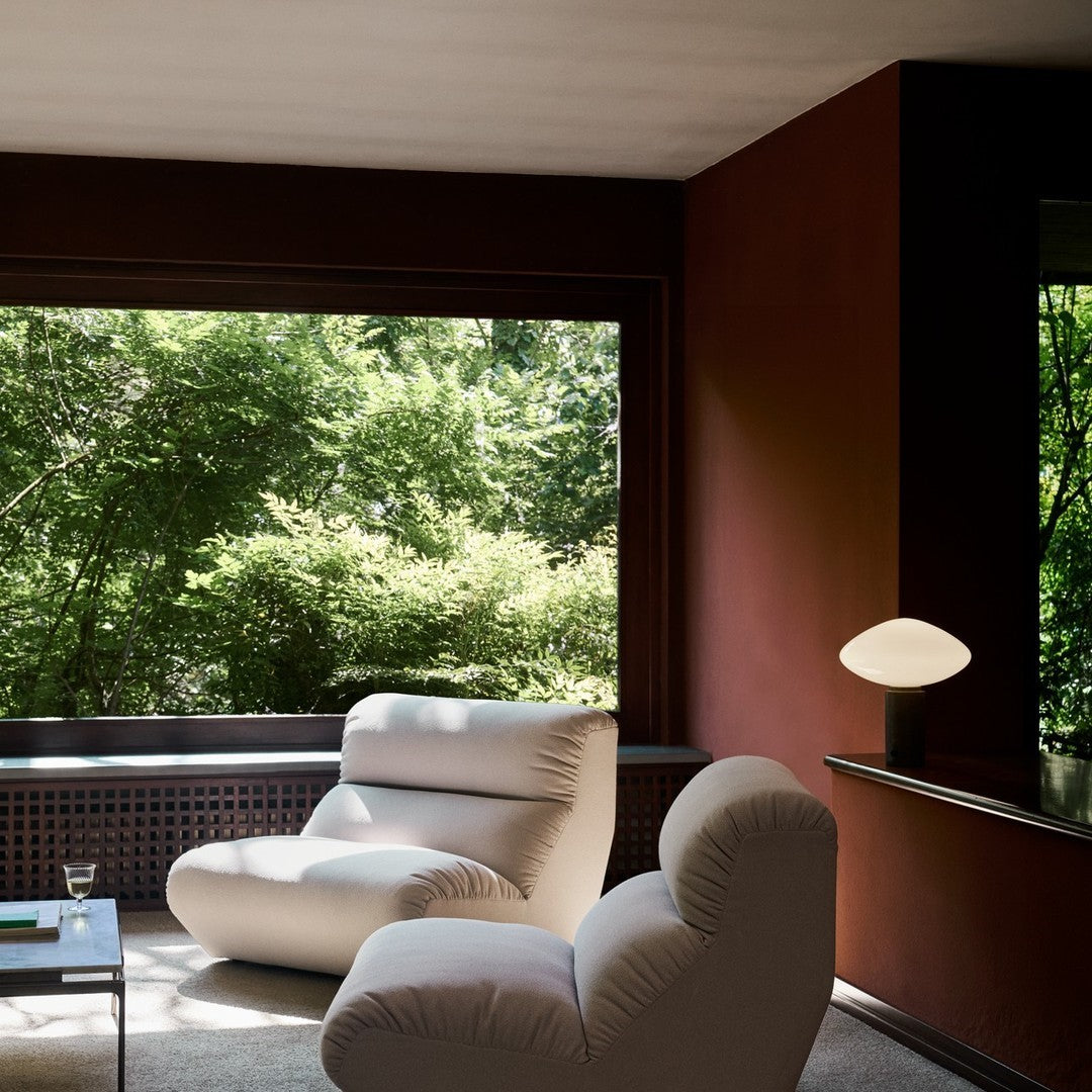 Modern lounge area featuring soft beige chairs and rich burgundy walls, complemented by greenery outside the window.