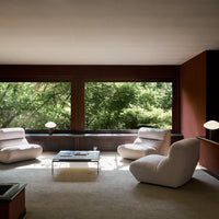 Light gray modern armchairs set against rich earthy red walls, framed by lush green foliage outside.