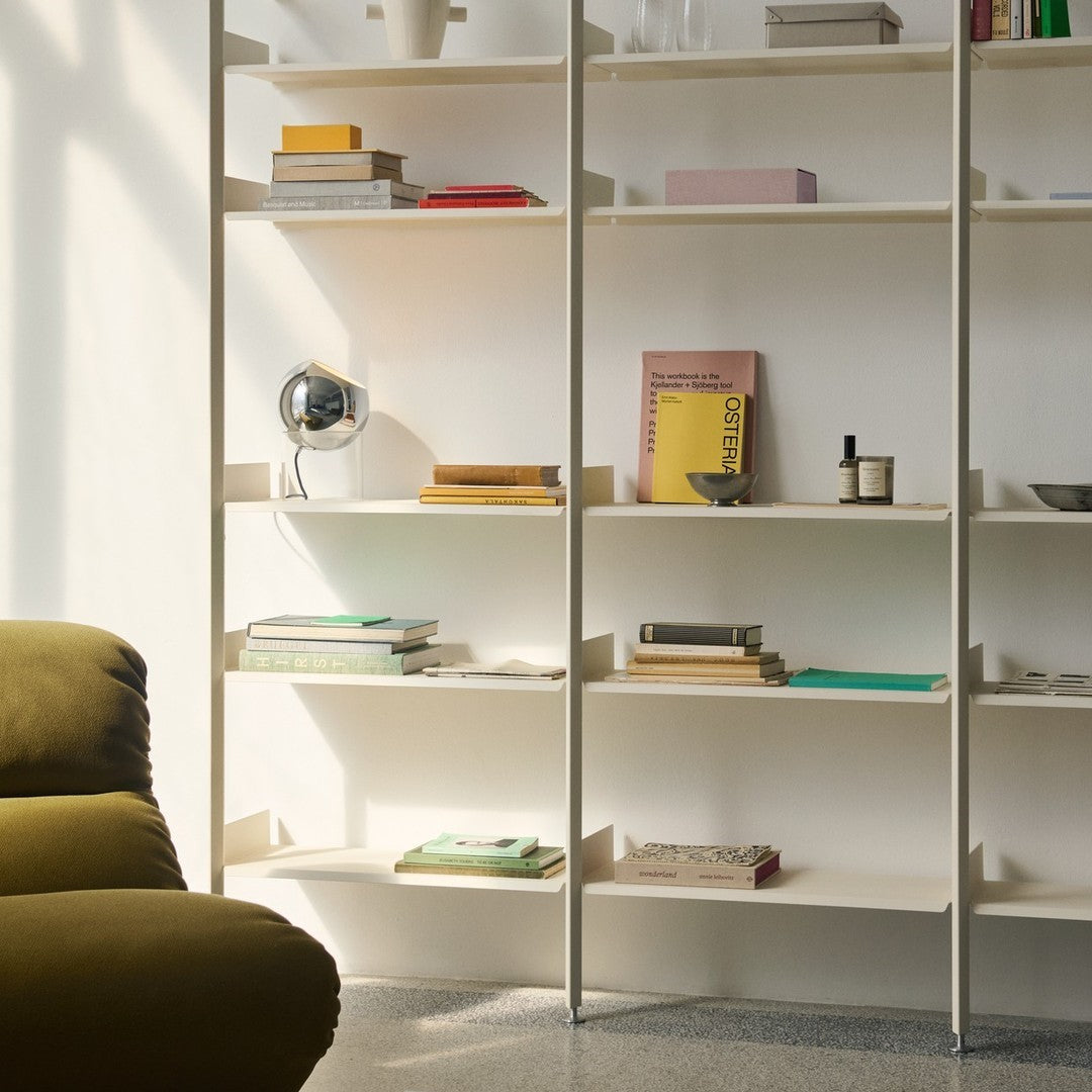 Modern bookshelf featuring neutral white shelves, brown and green accents, and colorful book covers in soft tones.