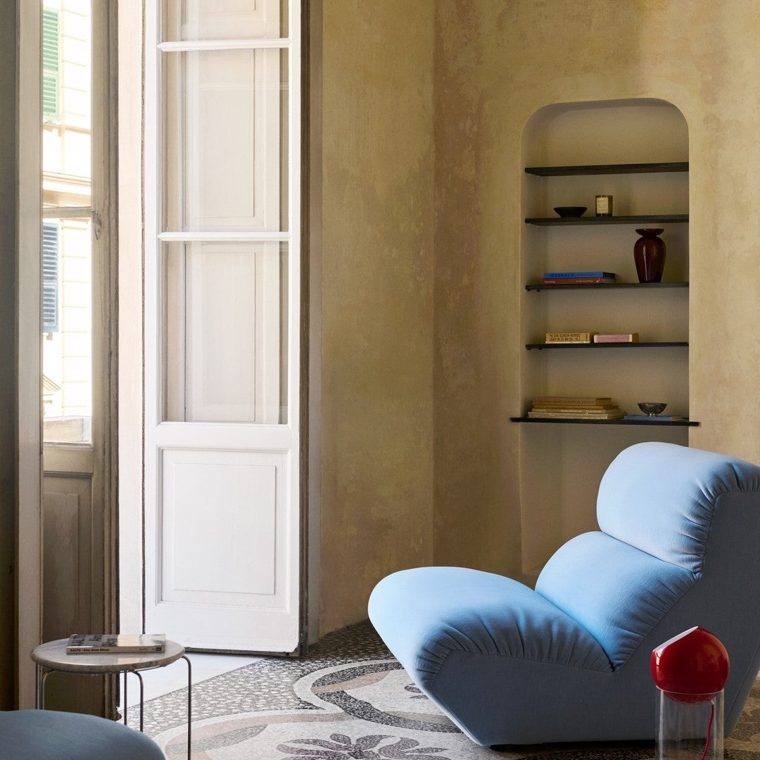 Blue curved sofa with soft fabric, against beige walls and patterned floor, featuring subtle black and red accents.