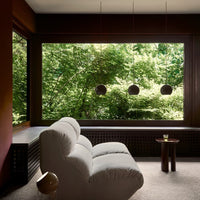 Light gray sofa with soft texture, surrounded by rich dark wood and lush green foliage through large windows.