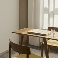Light wood table with soft yellow cushions, set in a neutral-toned, bright space. Patterns on the table's surface are minimal.
