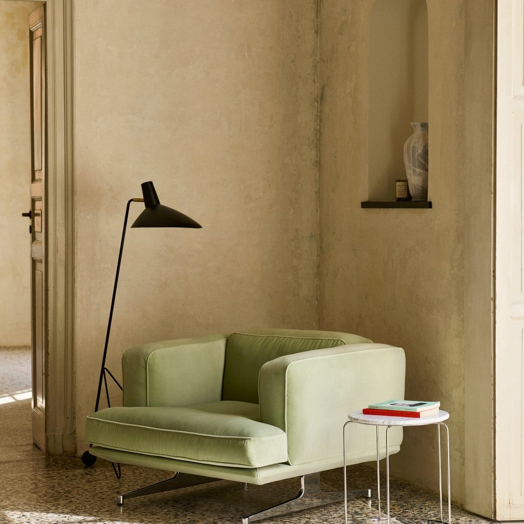 Soft green armchair with a minimalist design against a neutral beige wall, complemented by black and white accent pieces.
