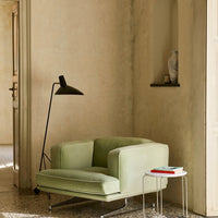 Soft green armchair with a minimalist design against a neutral beige wall, complemented by black and white accent pieces.