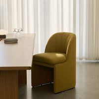 Modern curved chair in olive green with textured fabric, placed by a natural wood dining table.