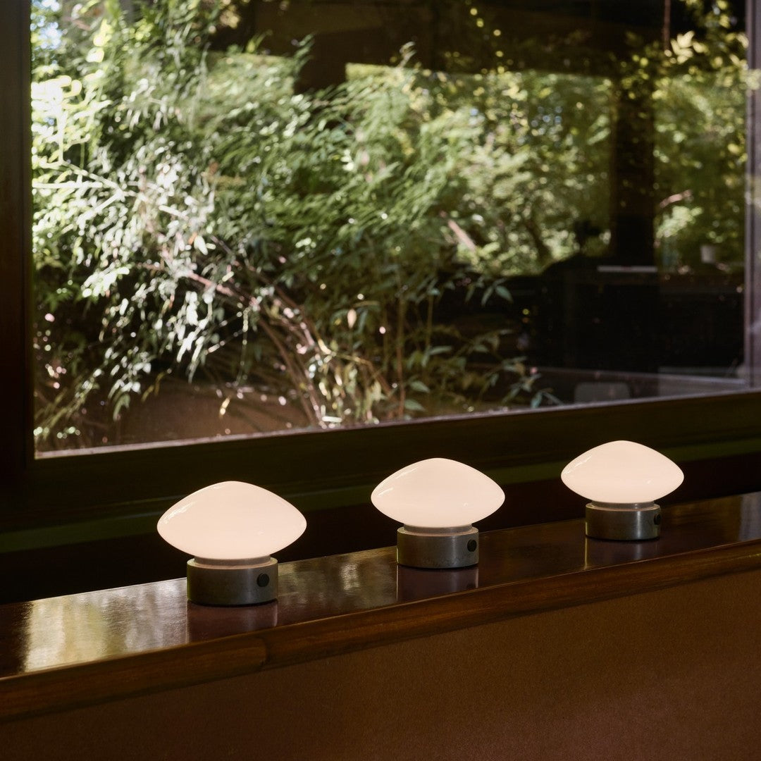 Three elegant white dome-shaped lamps on a wooden surface, surrounded by lush green foliage outside.