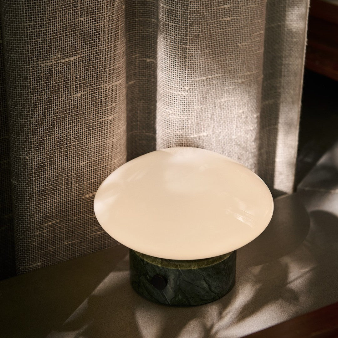 Glossy white lamp shade atop a dark green marble base, with soft textures and neutral gray backdrop.
