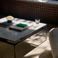 "Modern coffee table with a white marble top, green and blue books, and a clear glass, set on a beige carpet."