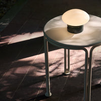 Modern round table in soft white with a marble base, topped by a glowing frosted glass lamp, showcasing subtle shadows.