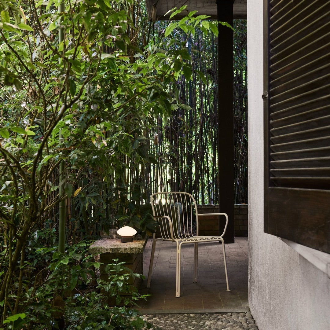 White metal chair on a stone patio surrounded by lush green foliage and textured wooden accents.