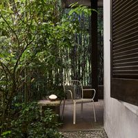 White metal chair on a stone patio surrounded by lush green foliage and textured wooden accents.