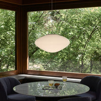 White pendant light above a round marble table, surrounded by deep blue chairs and lush green foliage outside.