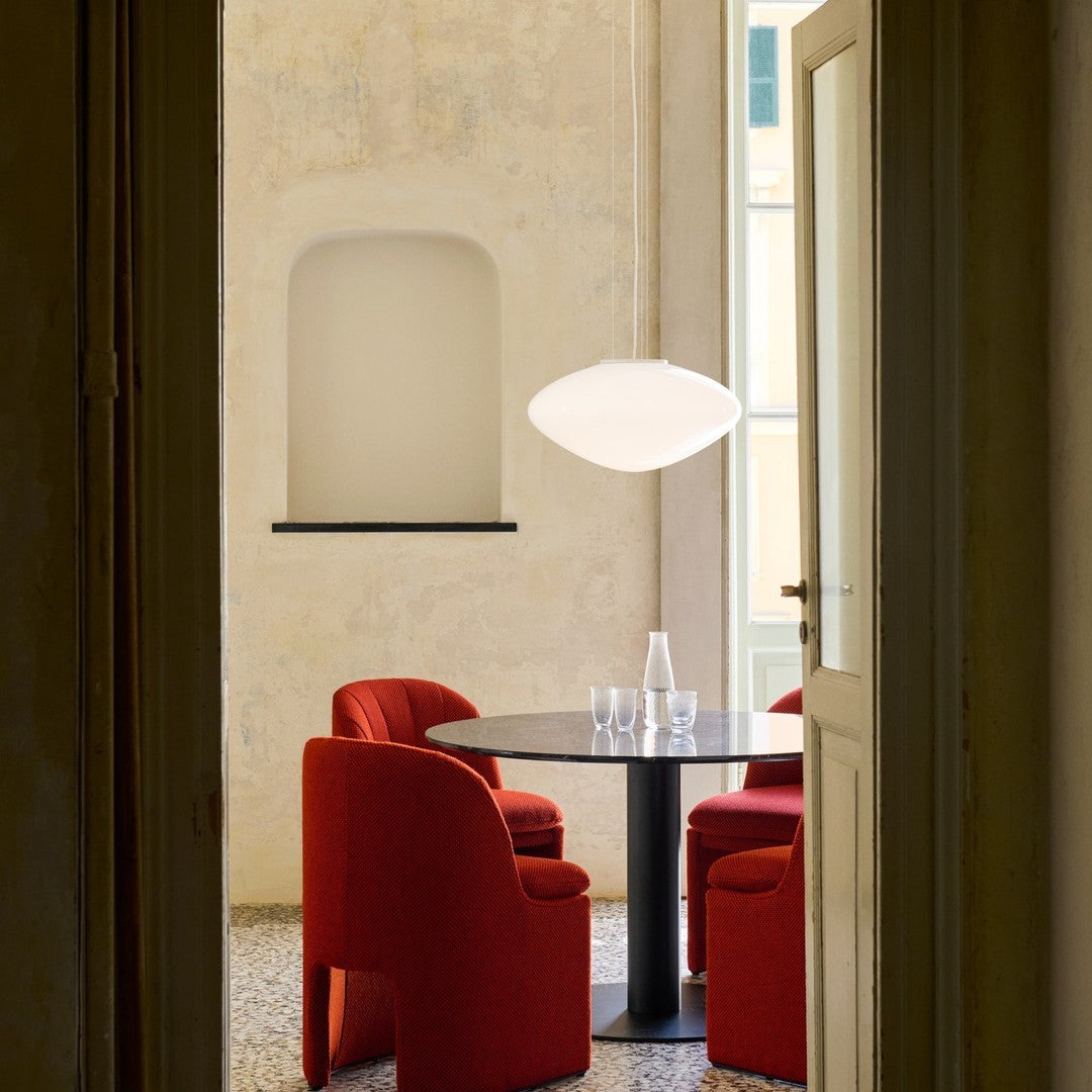 Red upholstered chairs around a black table with a white pendant light in a soft, neutral-toned room.