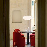 Red upholstered chairs around a black table with a white pendant light in a soft, neutral-toned room.
