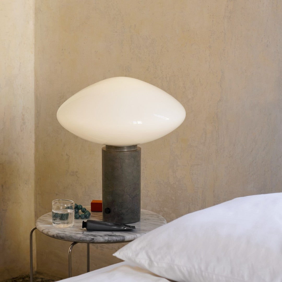 White glass lamp on a gray marble base, set against a soft beige wall, complemented by subtle textured patterns.