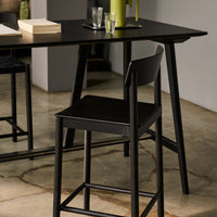 Black wooden chair with sleek design, set against a neutral-toned backdrop and a dark table surface. Glass accents visible.