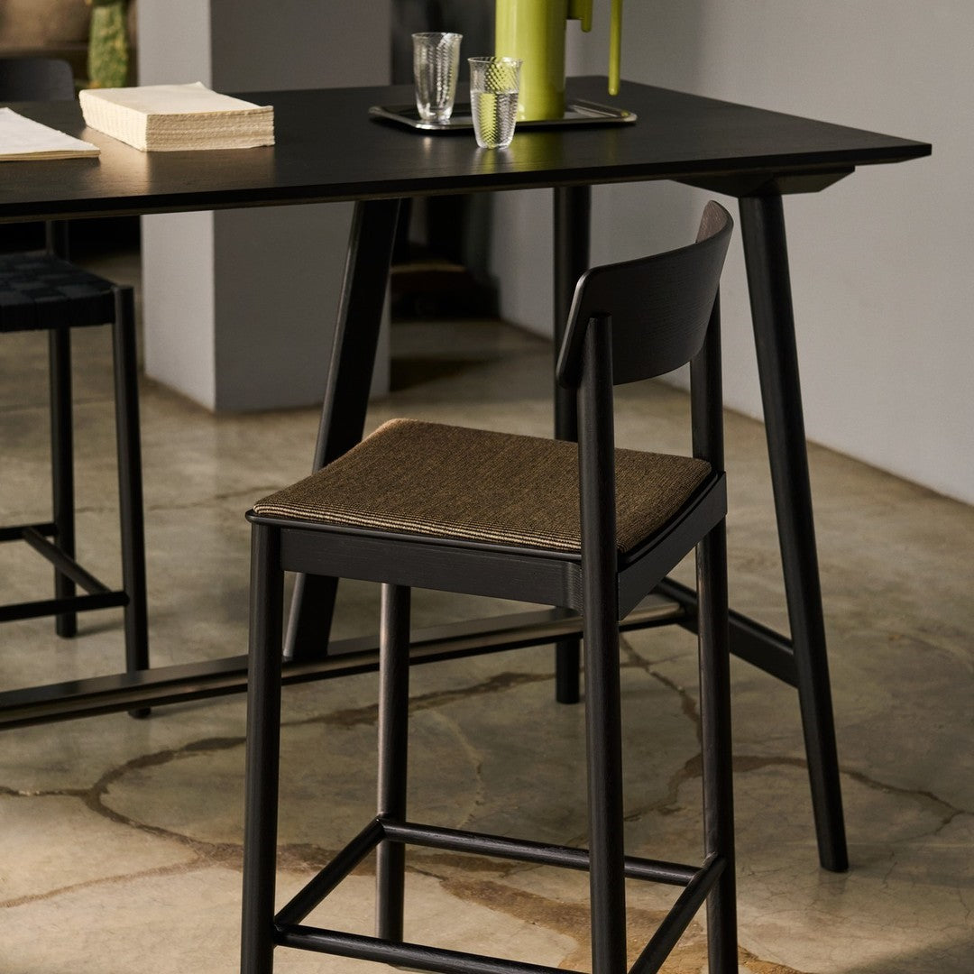 Black wooden table with muted tan and dark blue patterned chair cushions. Green pitcher adds a pop of color.