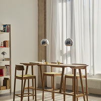 "Minimalist kitchen scene featuring chrome pendant lights, warm wood tones, and soft yellow seat cushions."