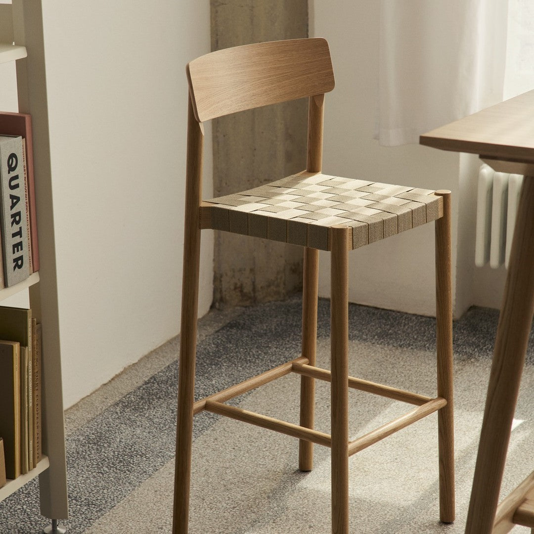 Natural wood bar stool with a woven beige and cream patterned seat, enhancing modern interior aesthetics.