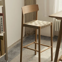 Natural wood bar stool with a woven beige and cream patterned seat, enhancing modern interior aesthetics.